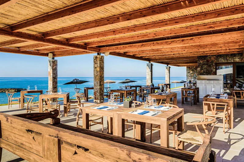 Outdoor seaside restaurant at Abaton Island Resort with wooden tables, chairs, and ocean view.