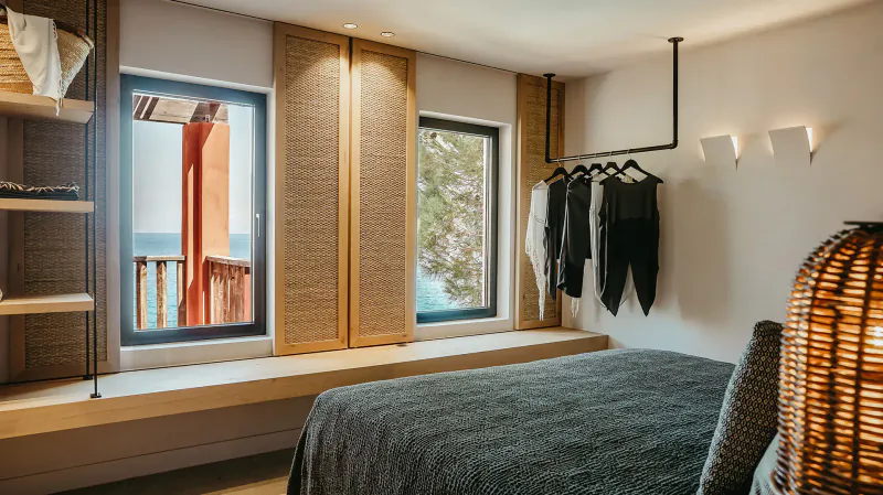 Cozy bedroom in Candia Park Village, Crete, with sea-view window, rattan shelves, black clothes on rack, and woven decor.