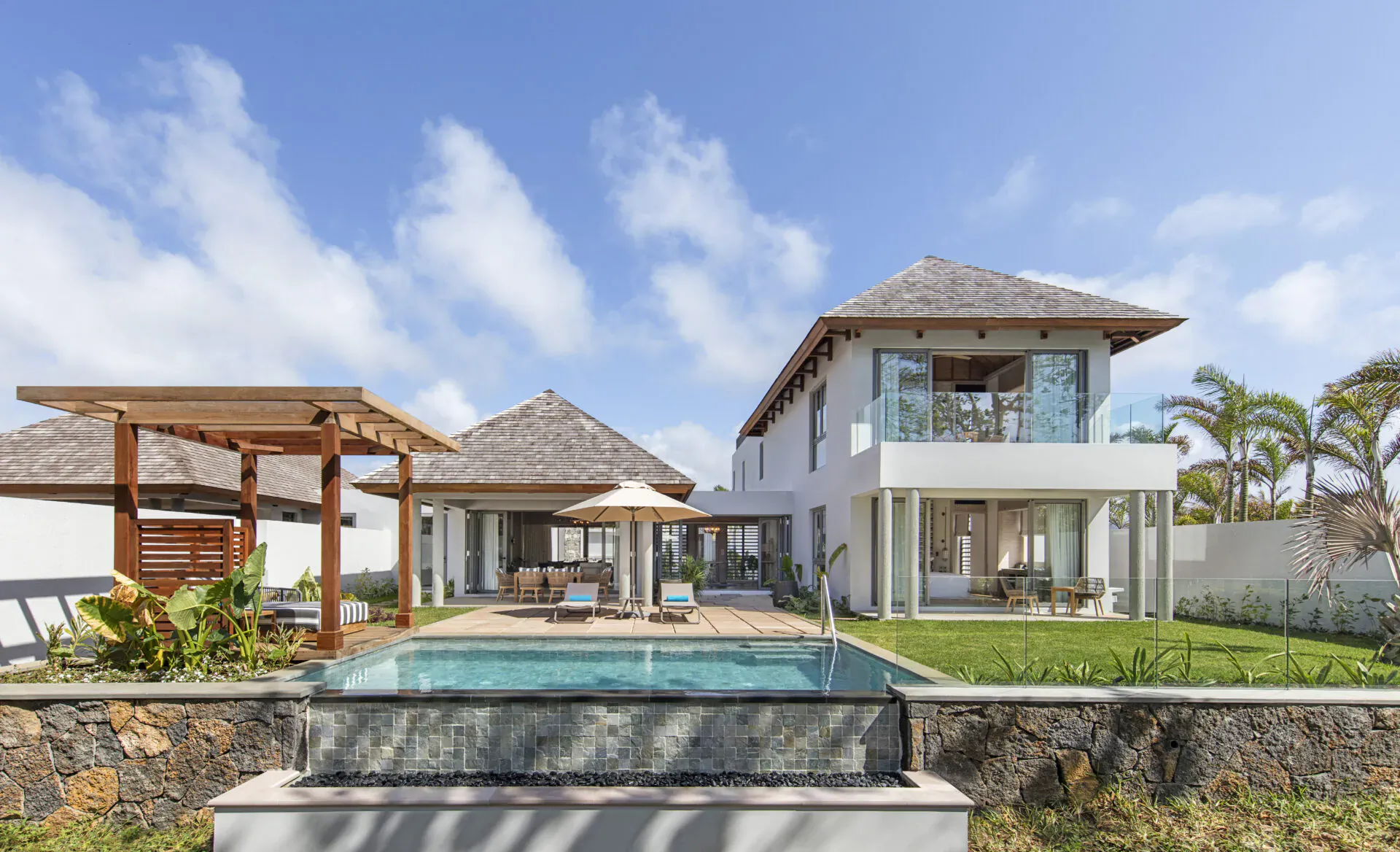 Modern white two-story villa with infinity pool, wooden pergola, palms, and blue sky at Anantara Iko Mauritius Resort