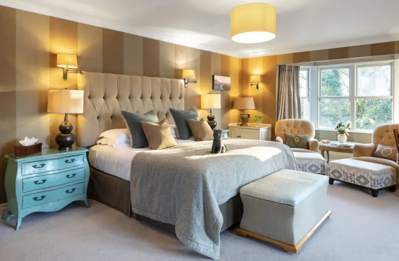 Elegant hotel bedroom at Gilpin Hotel with striped walls, king bed, teal chest, lamps, and window view.