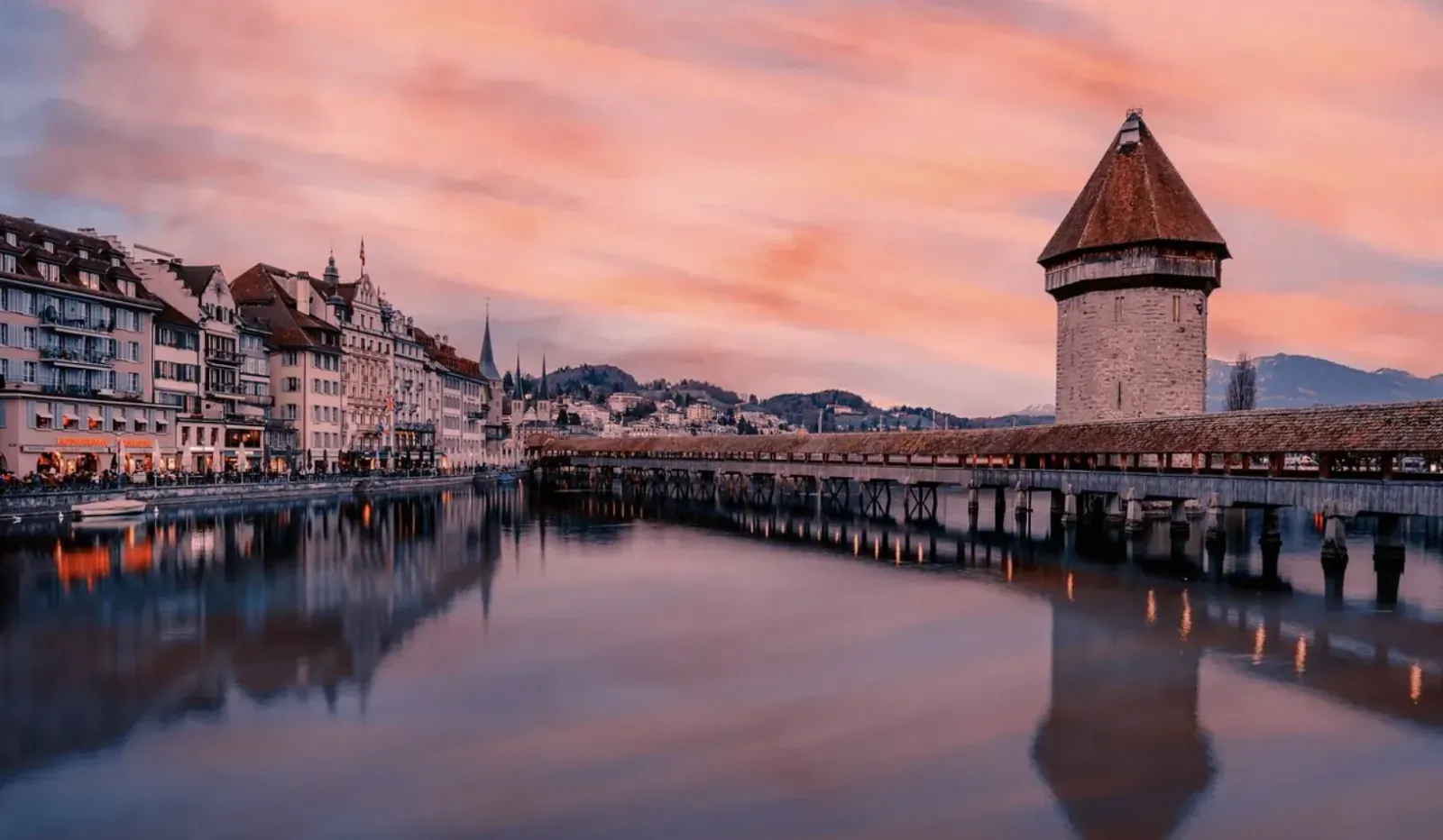 Chapel Bridge and Water Tower in Lucerne, Switzerland, at sunset with pink sky and river reflections