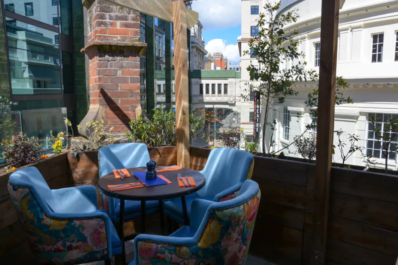 CoqBull Soho outdoor terrace with blue floral armchairs around orange placemat table, city skyline view