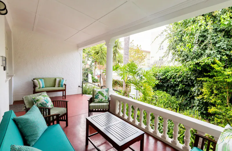 Spacious outdoor veranda at Eendracht Hotel with green cushions on white furniture, wooden table, and lush garden view.