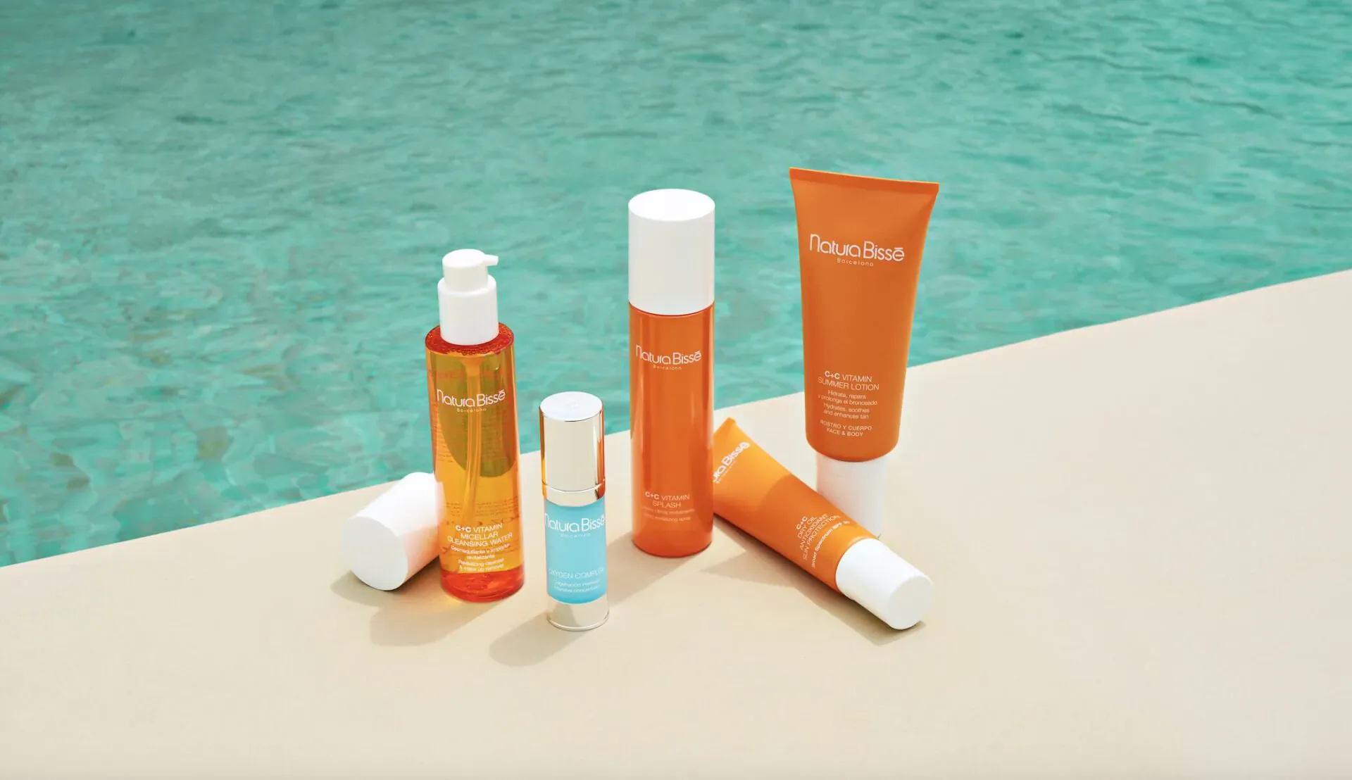Natura Bissé sun protection products: orange lotions, serums, and creams on surface by pool.