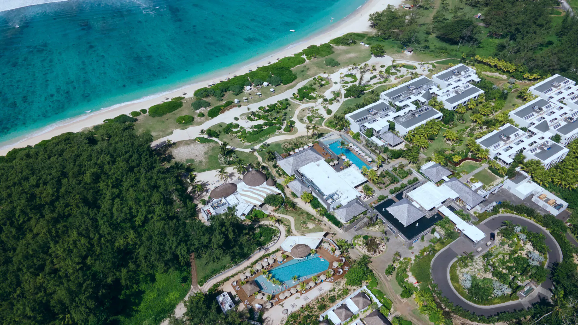 Aerial view of Anantara Iko Mauritius resort: white villas, infinity pools, lush gardens, and turquoise beachfront.