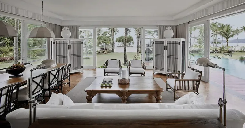 Spacious luxury living room at The Sanchaya with white sofa, wood table, bar stools, opening to tropical pool view.