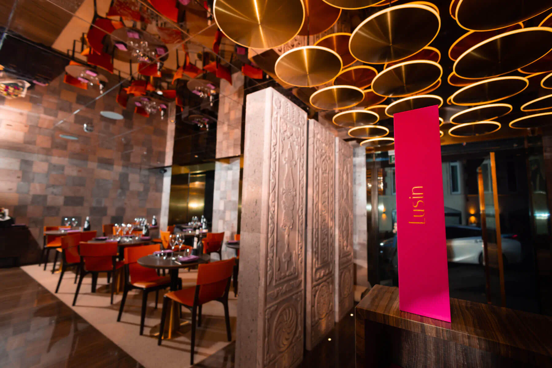 Lusin Mayfair Armenian restaurant interior with red chairs, tables, ornate gold ceiling discs, and pink 'Lusin' sign.