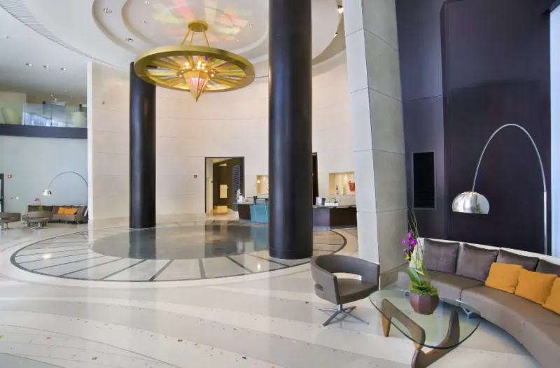 Elegant hotel lobby with grand chandelier, curved seating, orchids, reception desk, and modern arc lamps.