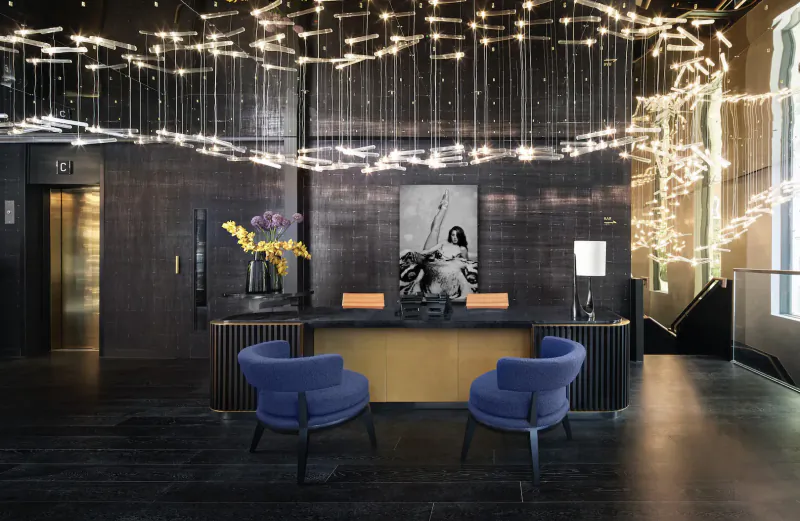 Luxurious Amano Hotel lobby with sparkling ceiling lights, yellow flowers, black-and-white photo, gold desk, blue chairs, elevator.