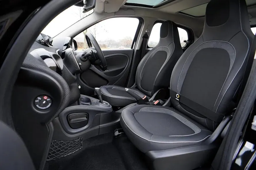 Spacious black leather interior of compact car with sport seats, open door, and panoramic roof.