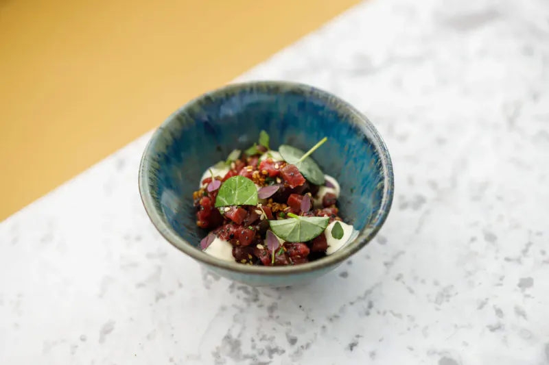 Close-up of beetroot salad with red beets, green herbs in a blue bowl on white marble surface