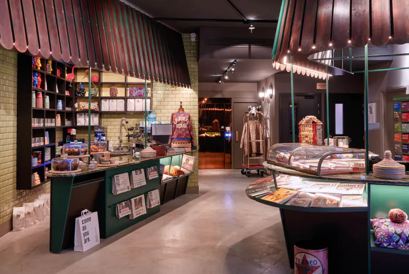 Cozy sustainable gallery shop in Paris with green shelves stocked with books, candies, displays, and cafe counter.