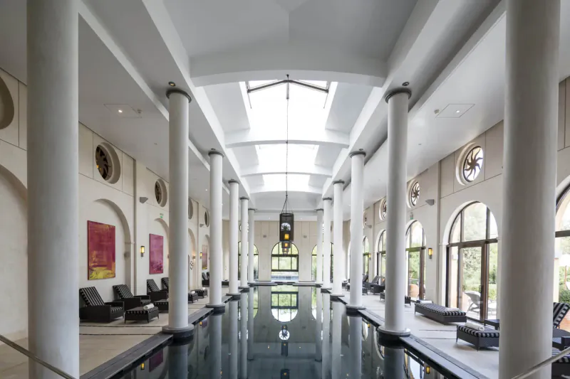 Elegant indoor pool gallery at Terre Blanche in Provence with white columns, skylight, and loungers.
