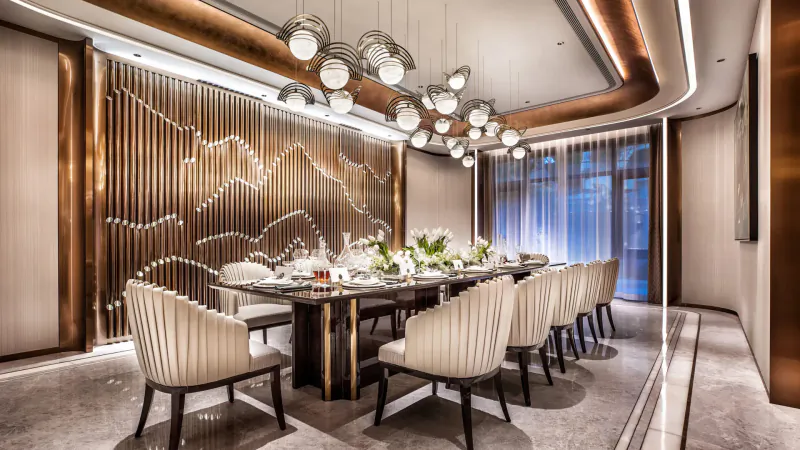 Elegant dining room with long dark wood table, white upholstered chairs, floral centerpiece, metallic wavy wall, globe pendant lights, large windows.