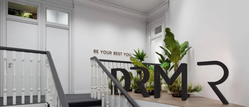 Modern white hallway with large black DRMR letters, potted plants, stairs, and 'BE YOUR BEST' text on wall