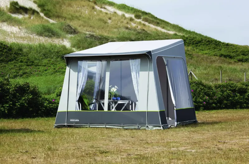 Grey Isabella motorhome awning tent with open windows, table, chairs, and flowers, set on grassy dunes.