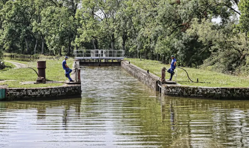 Tree-lined canal lock in Burgundy with blue-uniformed workers on stone walls and bollards