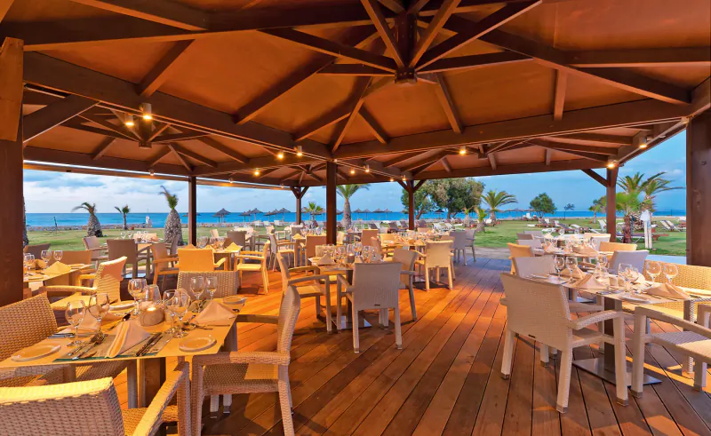 Spacious open-air beachfront restaurant at Cavo Spada resort in Crete, with wooden tables set for dining under a pergola overlooking the sea.