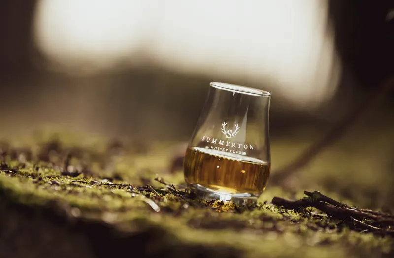 Summerton whisky in a Glencairn glass on mossy forest floor, soft bokeh background.