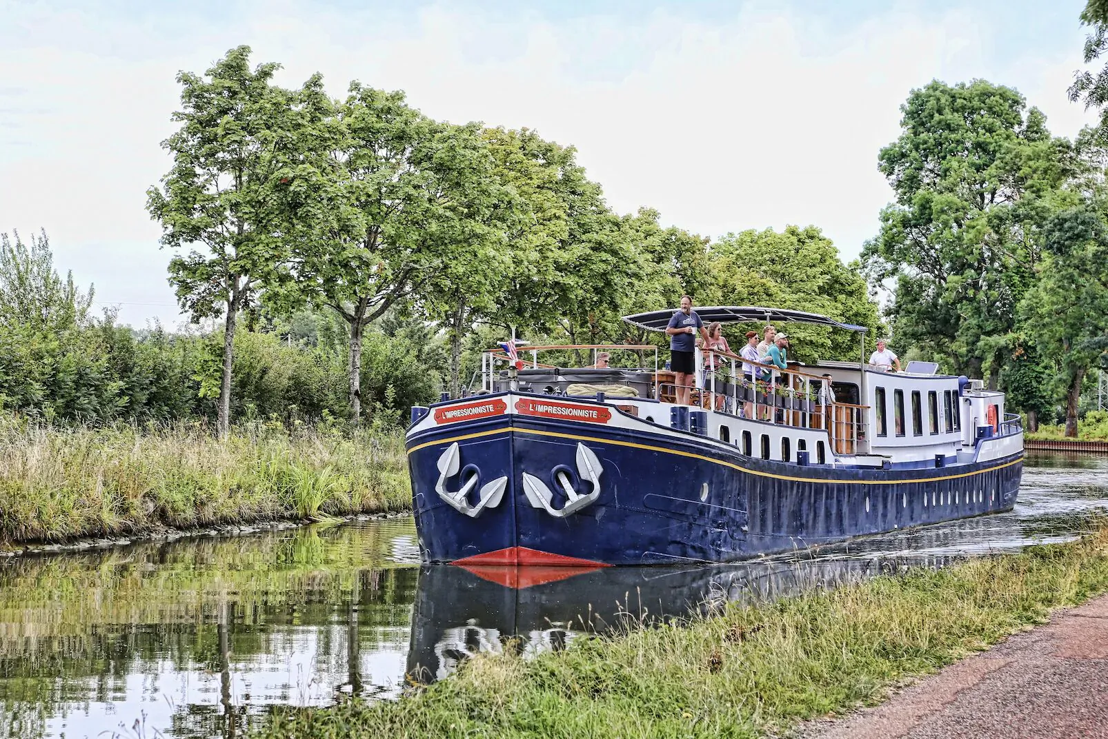 Blue canal boat with anchors and 'Burgundy in Motion' cruises tree-lined waterway in France's wine country