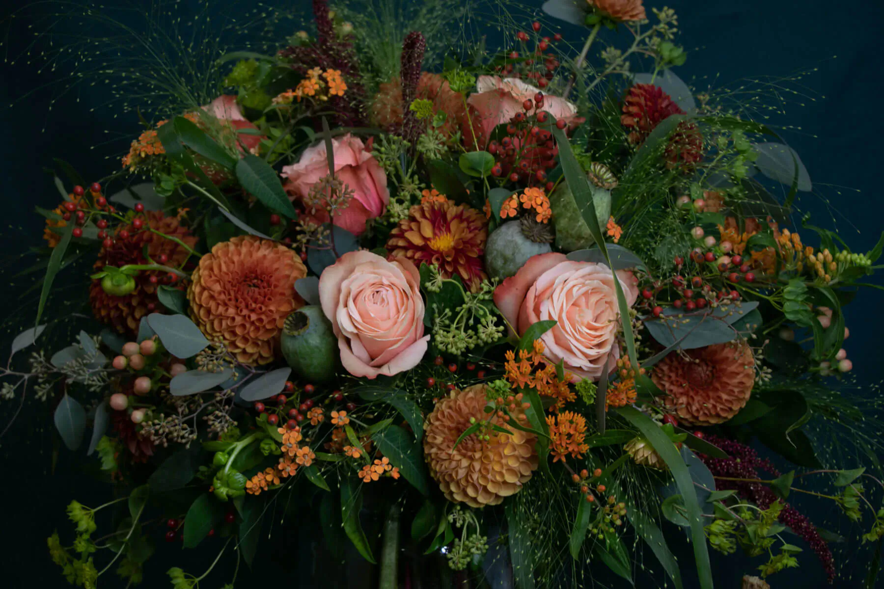 Vibrant bouquet of pink roses, orange dahlias, eucalyptus, and berries on dark background