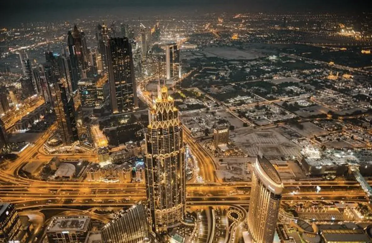 Aerial night view of Burj Khalifa and glittering Dubai skyline with highways and skyscrapers.