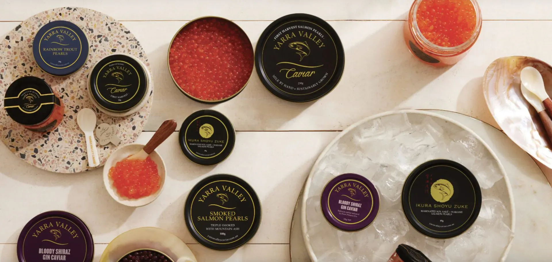 Assortment of Yarra Valley Caviar tins in black, blue, purple with orange roe, spoons, on white table at Harrods launch