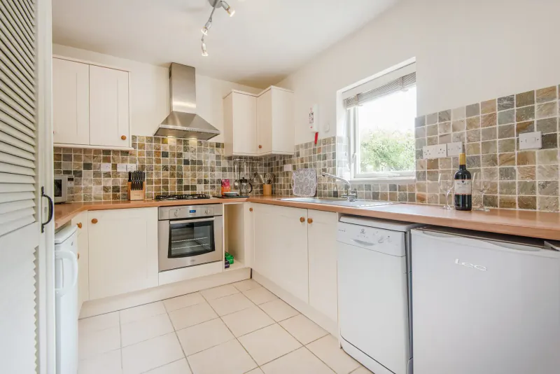 Modern white kitchen in Broomhill Manor with wooden counters, stainless hood, dishwasher, oven, and wine bottle on counter.