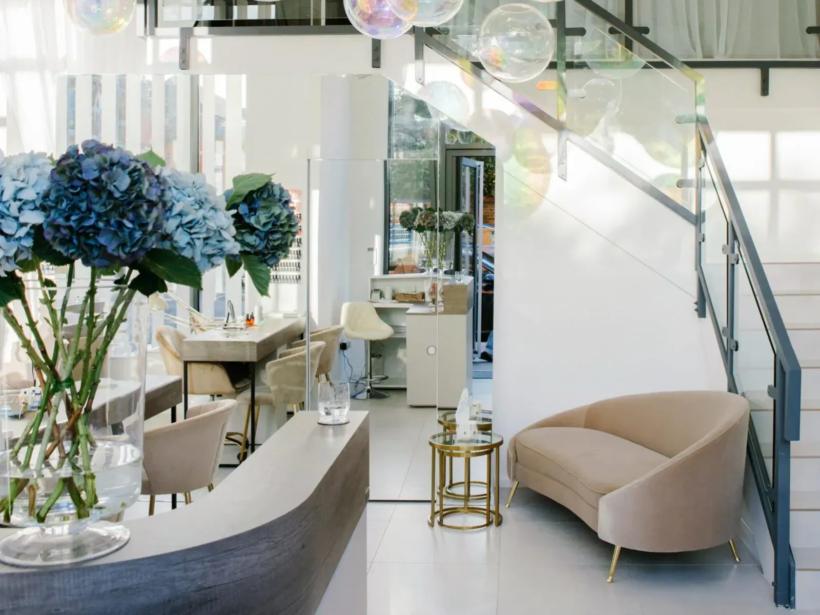 Skin Loft beauty salon interior with blue hydrangea arrangements, curved reception desk, beige chaise, and glass staircase