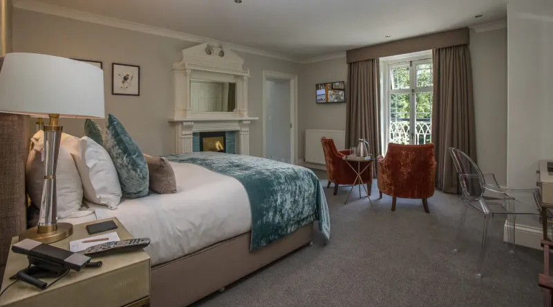 Elegant Rothay Manor hotel bedroom with teal bed, fireplace, orange armchairs, table, and window views.