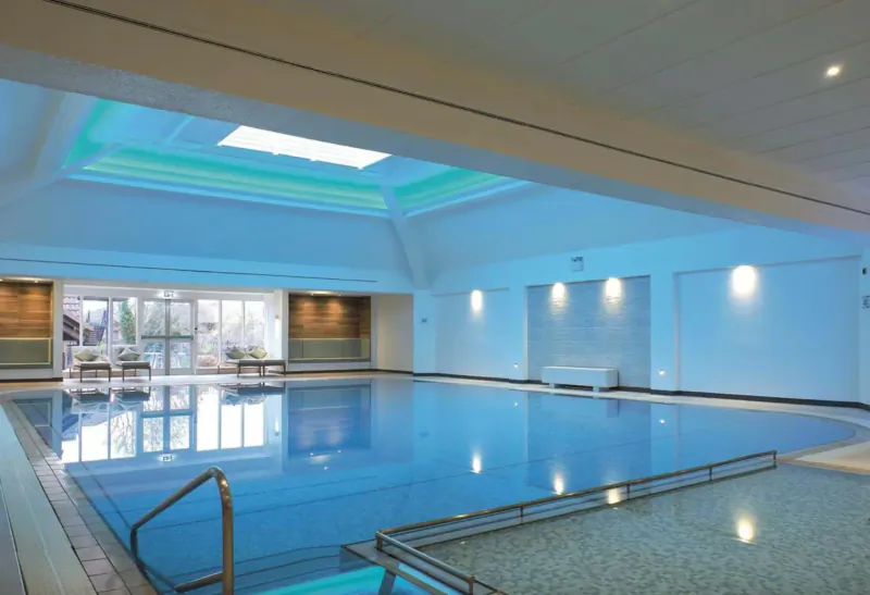 Indoor swimming pool at Aztec Hotel & Spa in Bristol, with lounge chairs, skylight, and elegant architecture.