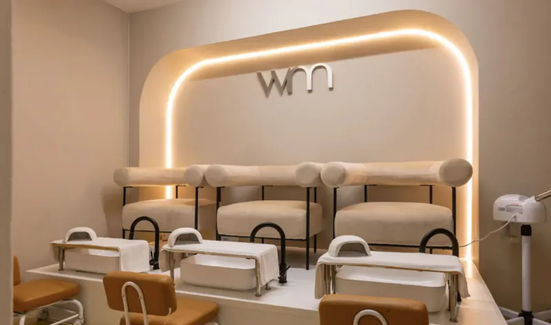 Wumman Spa nail salon interior with curved neon 'WnN' sign above four beige pedicure chairs and UV lamps.