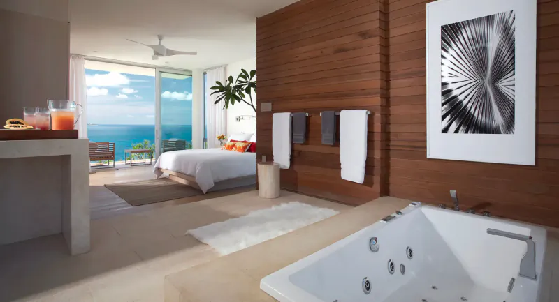 Luxurious private resort bedroom and bathroom with ocean view, jacuzzi tub, towels, and abstract art.