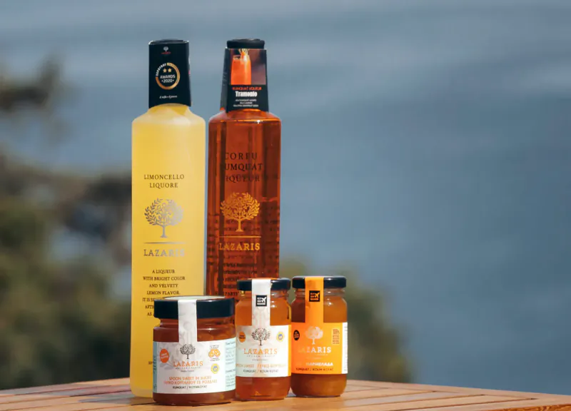 Assortment of Angsana olive oil bottles and jars on wooden table overlooking the sea at Corfu resort.