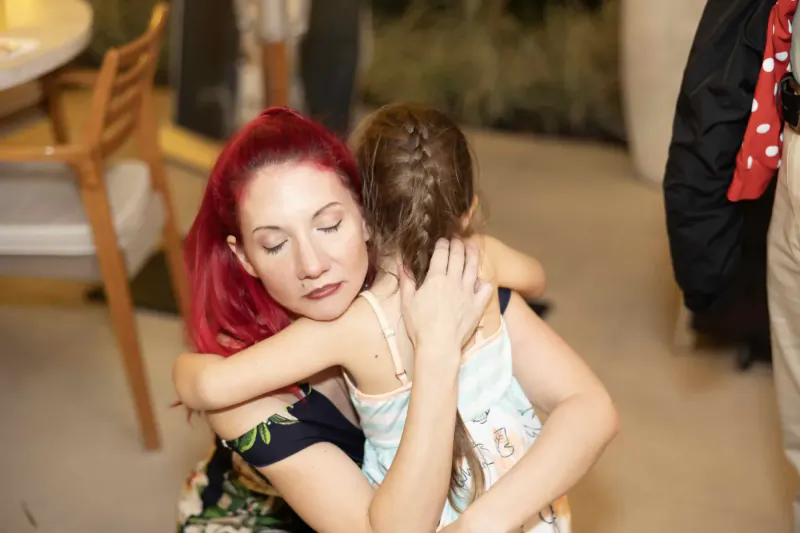 Red-haired woman warmly hugs young girl with braided hair in gallery setting