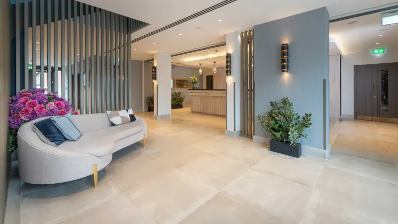 Modern hotel lobby with curved white sofa, purple flowers, plants, reception desk, and glass walls