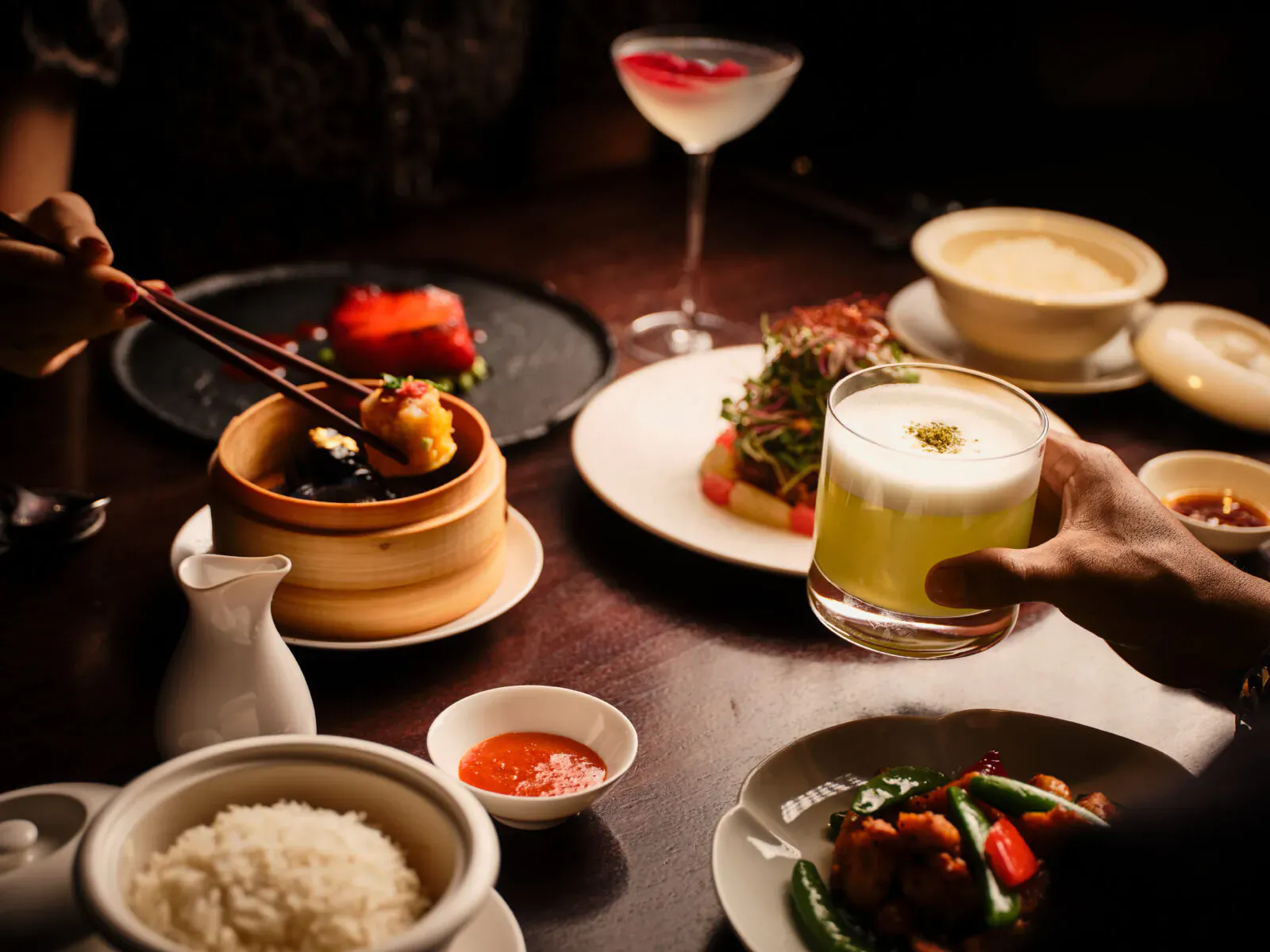 Close-up of Hakkasan Mayfair modern Cantonese dishes: dim sum, rice, stir-fry, soup, and a creamy cocktail on a dark table.