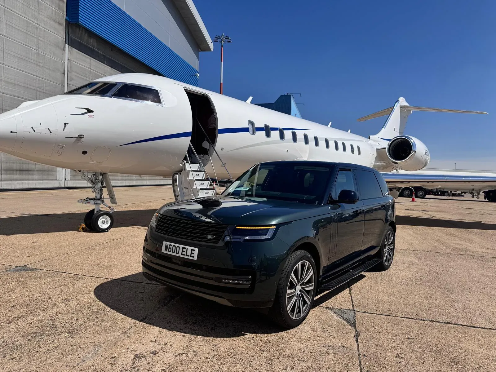 Dark green Range Rover Velar (plate KN73 ULE) parked beside white private jet with open door at airport hangar.