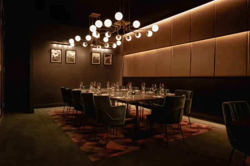 Elegant Gaucho restaurant interior in Cardiff: long wooden table with green chairs, orb chandelier, warm LED walls, framed art.