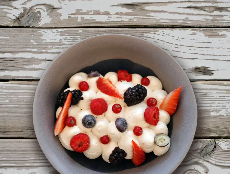 Gray bowl of white yogurt topped with strawberries, raspberries, blueberries, and blackberries on wooden surface