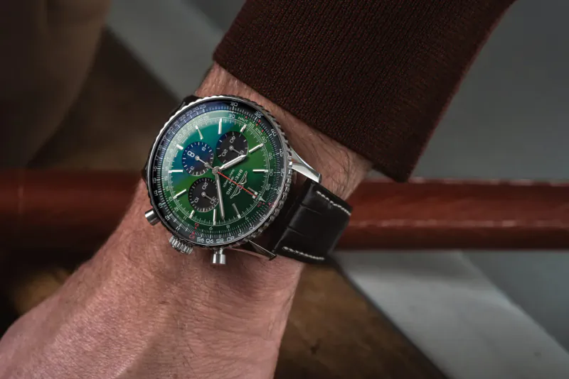 Close-up of Breitling Navitimer chronograph watch on man's wrist, green and black dial, brown leather strap