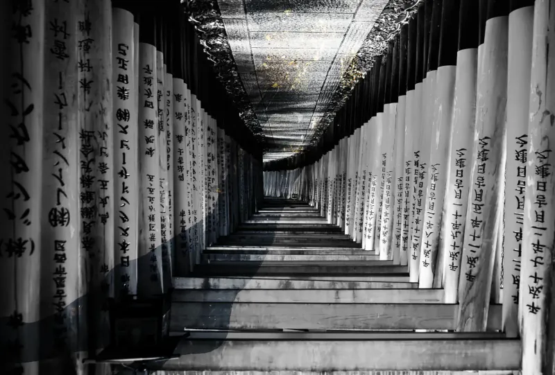 Black and white view down a long corridor lined with tall white pillars inscribed with Japanese text