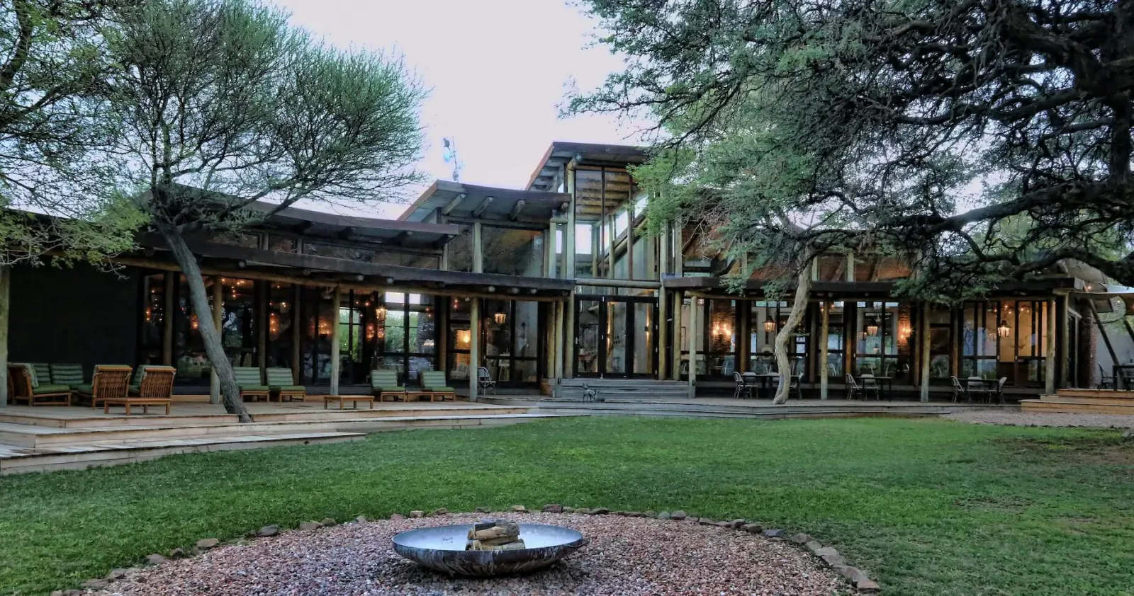 Marataba Game Lodge in Waterberg: modern wooden building with verandas, trees, lawn, and fire pit at dusk
