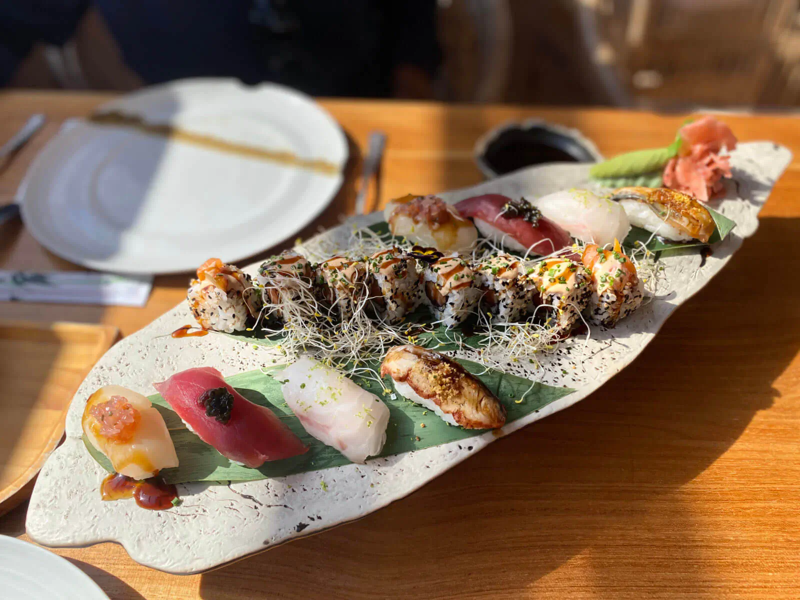 Assortment of sushi rolls, nigiri, and sashimi on a leaf-shaped white plate with garnishes on wooden table