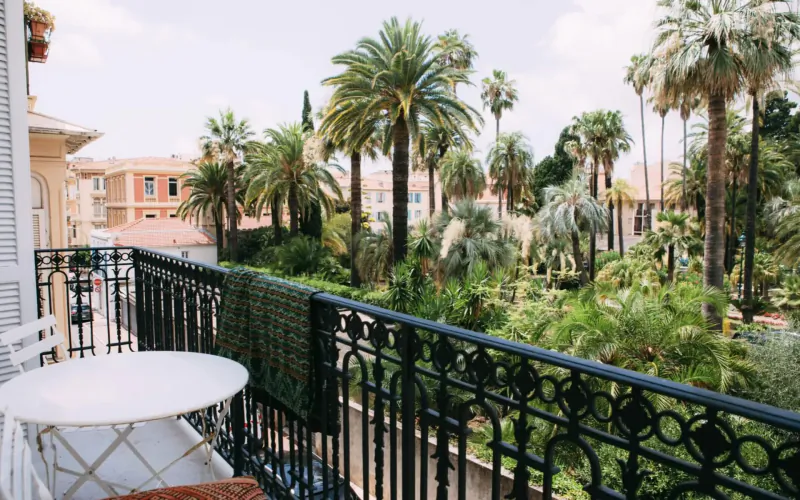 Balcony with round table overlooking lush palm trees and ochre buildings in tropical oasis setting
