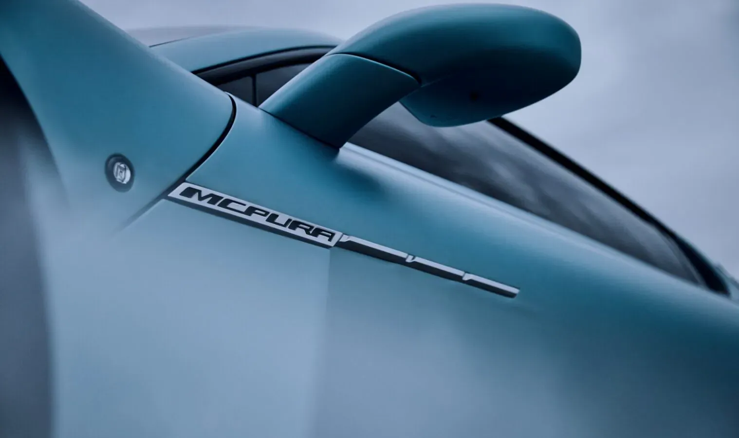 Close-up of teal Maserati MC Pura badge on sleek car body near side mirror