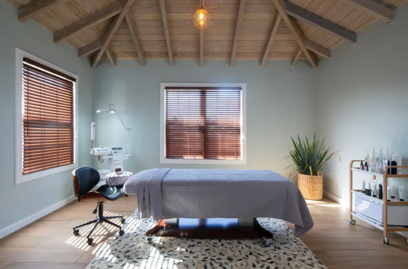 Luxurious massage room at Hammock Cove Antigua with blue massage table, wooden ceiling, plants, and therapy cart.