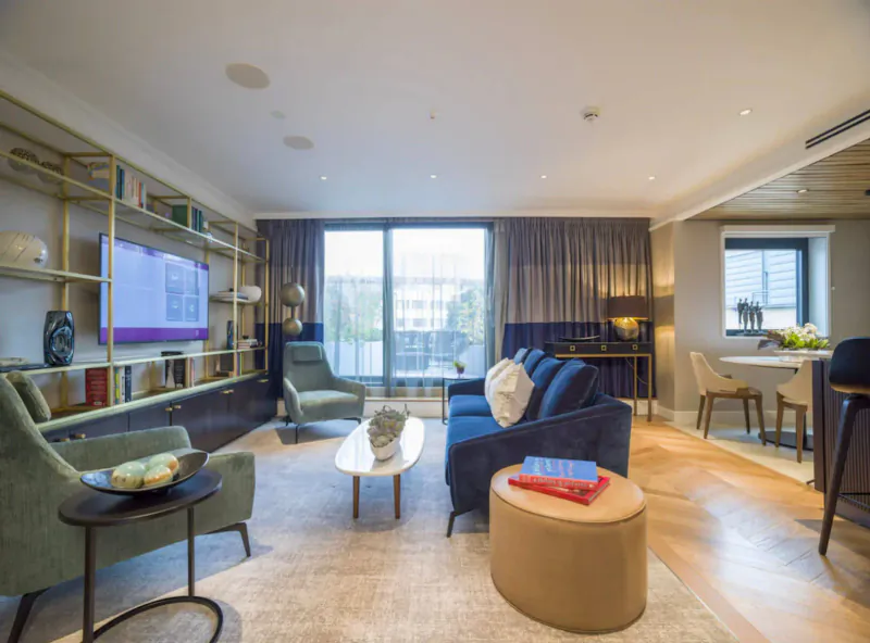 Elegant living room in The Guardsman boutique London hotel with navy sofa, gold bookshelves, plants, and balcony view.