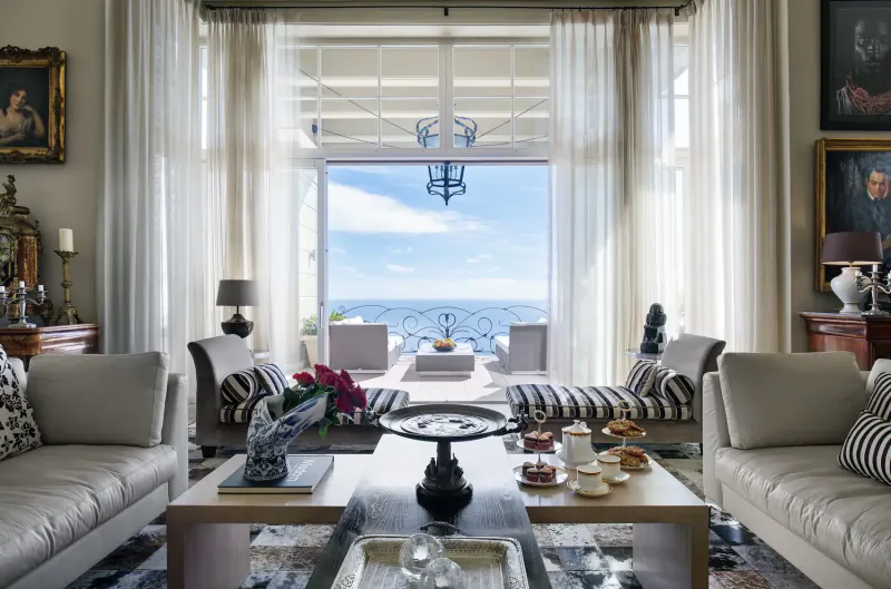 Elegant living room at 21 Nettleton in Clifton, Cape Town, with ocean view through French doors, plush sofas, coffee table with tea and pastries.