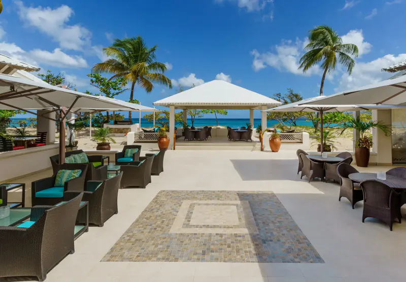 Spice Island Beach Resort in Grenada: open-air beachfront terrace with wicker furniture, umbrellas, palms, and ocean view.